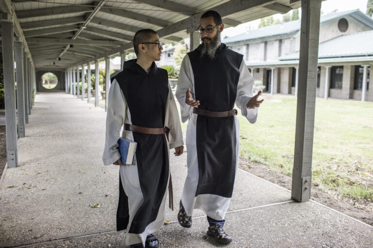 Two monks walk down a corridor conversing