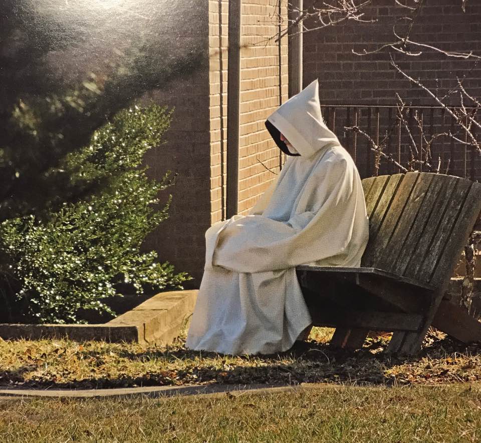 Trappist monk in cowl sitting on a bench